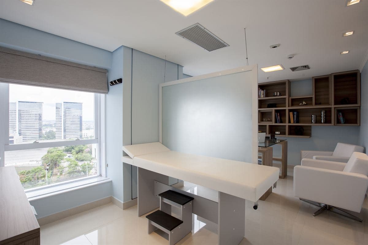 Sala de exame do consultório, com maca clínica junto à janela